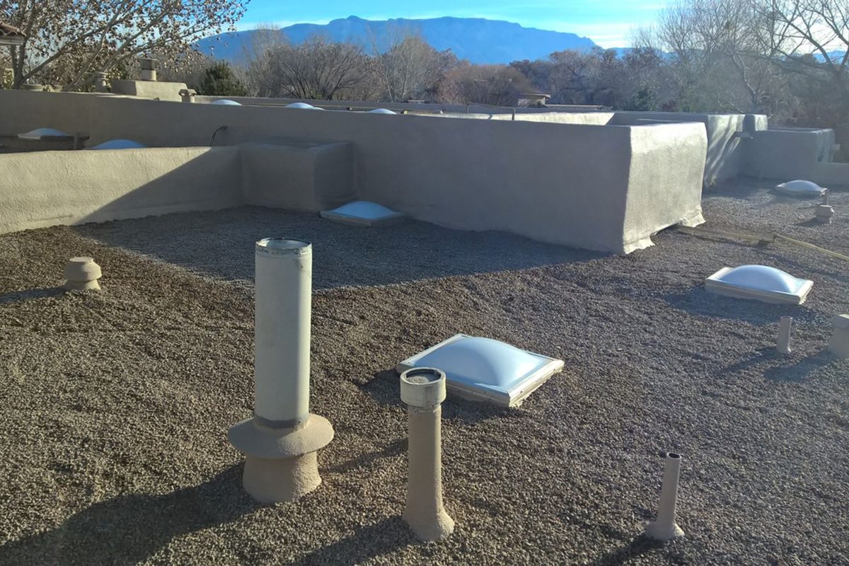 Flat roof of an Albuquerque home with coated parapet walls, skylights, and vents, Sandia Mountains behind
